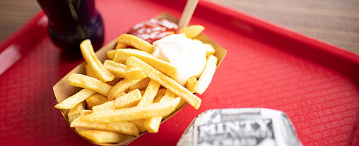 Auf dem Tablet liegt ein Buffalo Burger und Pommes mit Majo und Ketchup.