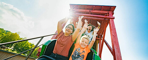 Beim Schulausflug reißen die Kinder in der Achterbahn die Arme hoch.