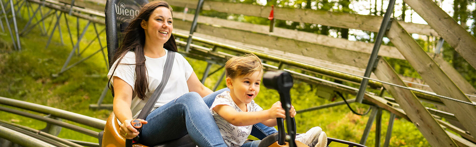 Mutter und Sohn rasen auf der Sommerrodelbahn den Berg hinab und haben viel Spaß dabei.