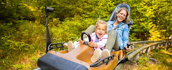 Dem kleinen Mädchen sieht man die Freude in der Sommerrodelbahn Trapper Slider mit ihrer Mutter deutlich an.