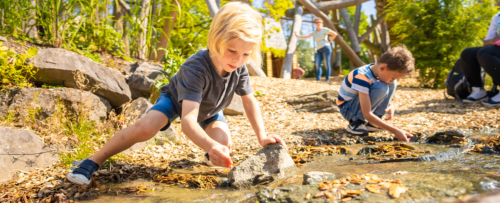 Die Kinder spielen am Bachlauf in der Adventure Area und entdecken die Natur.