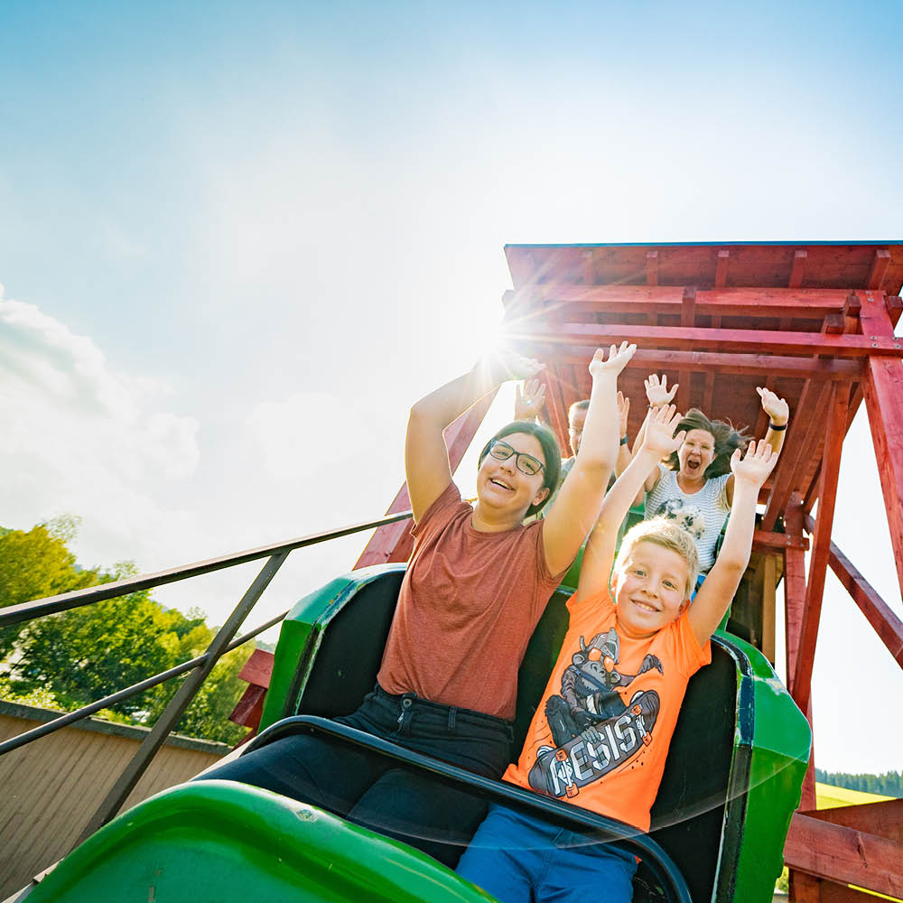 Beim Schulausflug reißen die Kinder in der Achterbahn die Arme hoch.