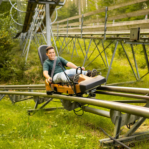 Auf der Sommerrodelbahn Trapper Slider rast der Junge den Berg hinunter. und hat viel Spaß.