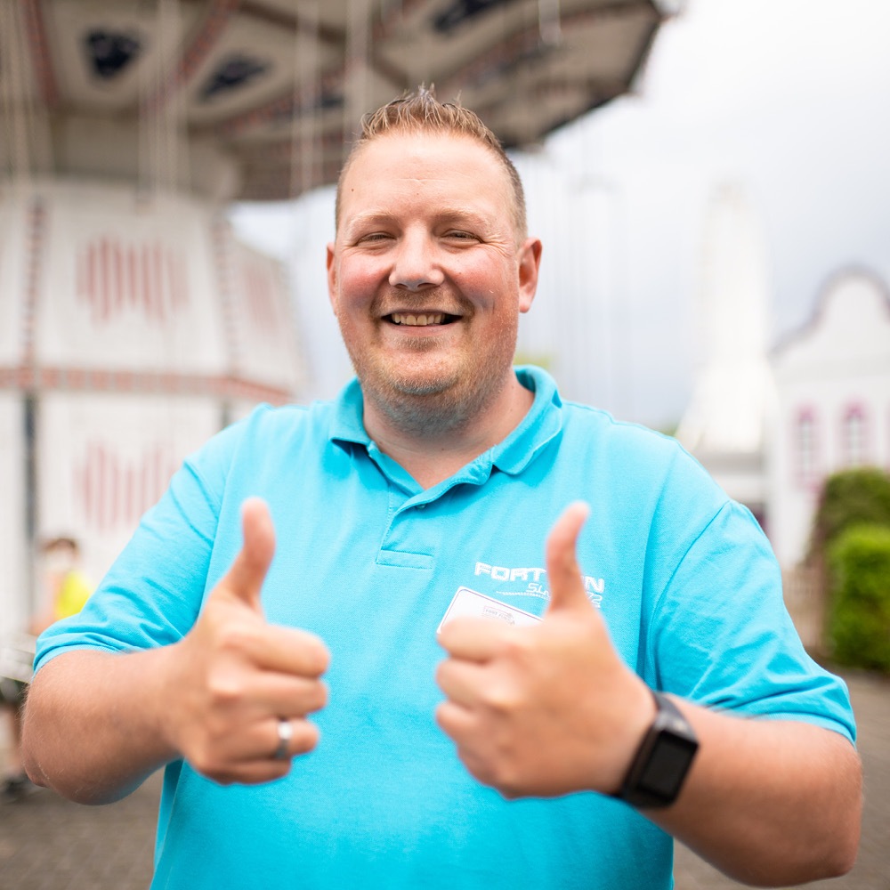 Der freundliche Mitarbeiter im Park zeigt mit seinem Lächeln beide Daumen hoch vor dem Wellenflieger.